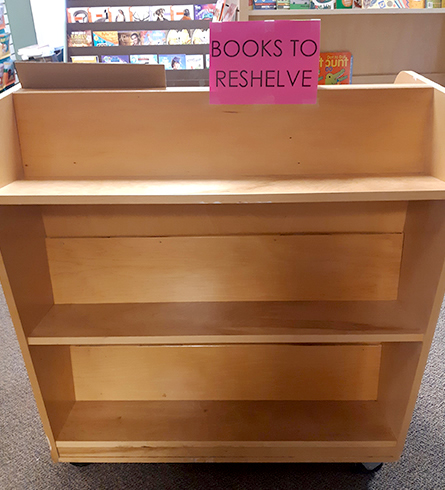 Cart with sign saying "Books to Reshelve"
